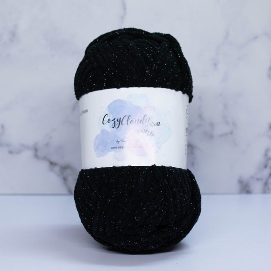 A skein of black yarn with a label that reads 'Cozy Cloud Cosmic Lite - 02 Black Hole'.