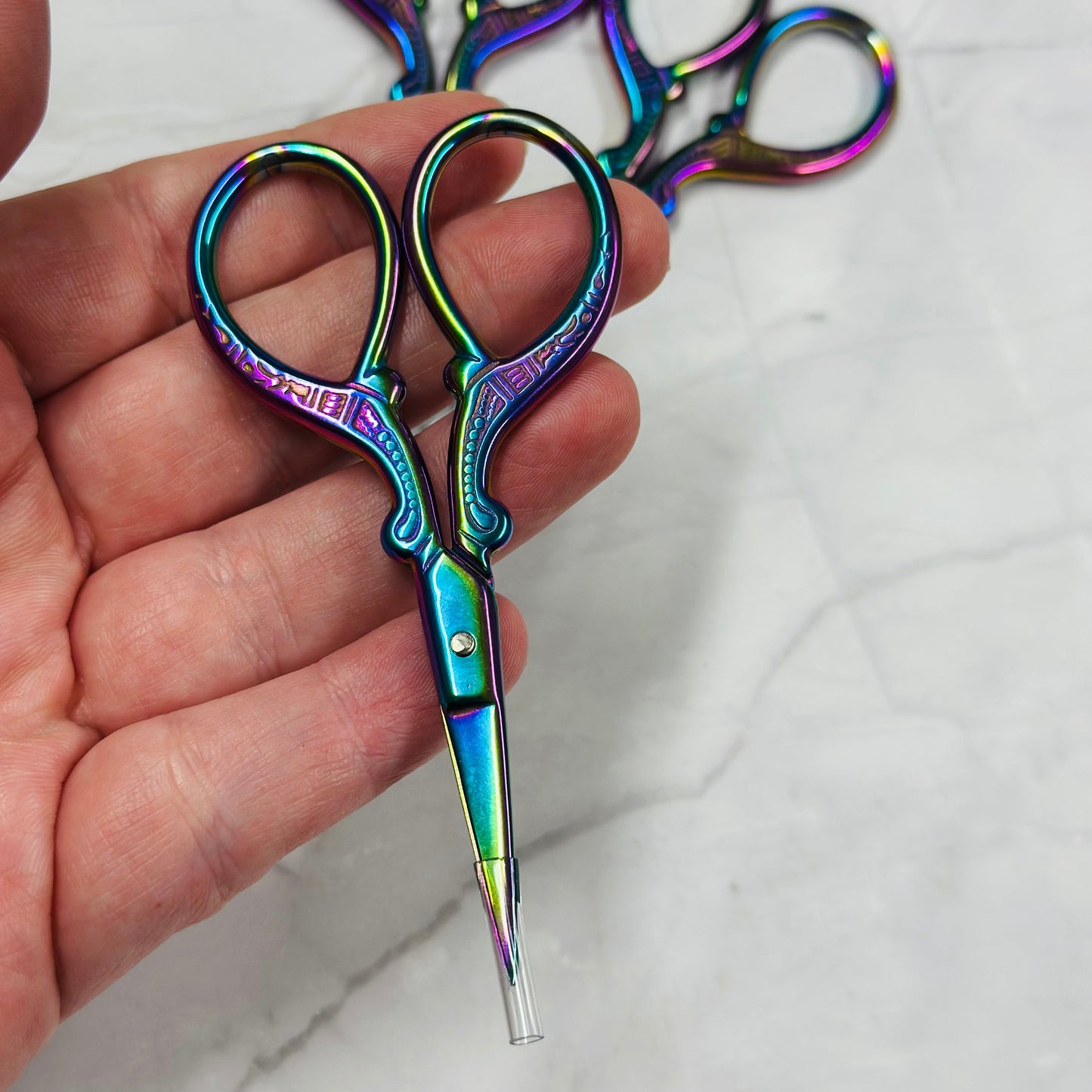 Hand holding a pair of colorful scissors with more scissors in the background on a light surface.