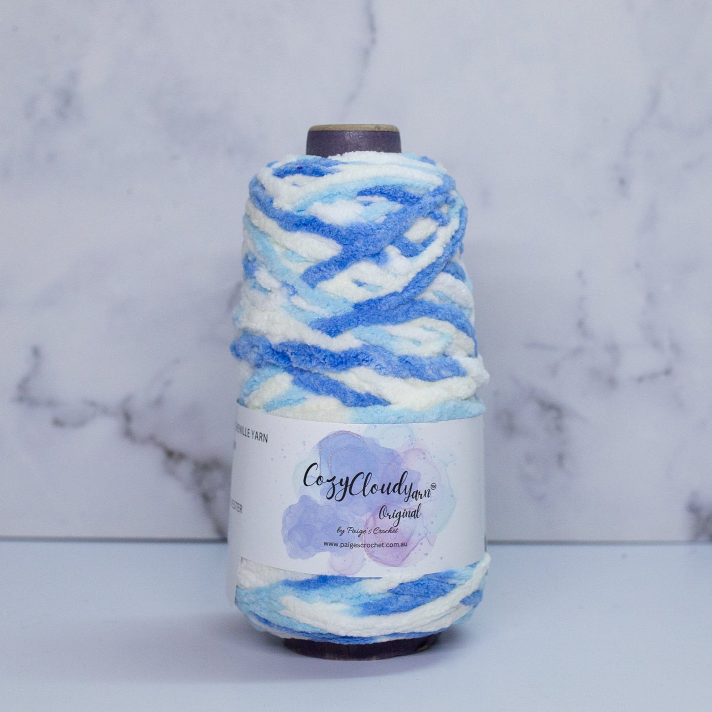 A spool of Cozy Cloud yarn in blue and white color blocks, placed against a marble background.