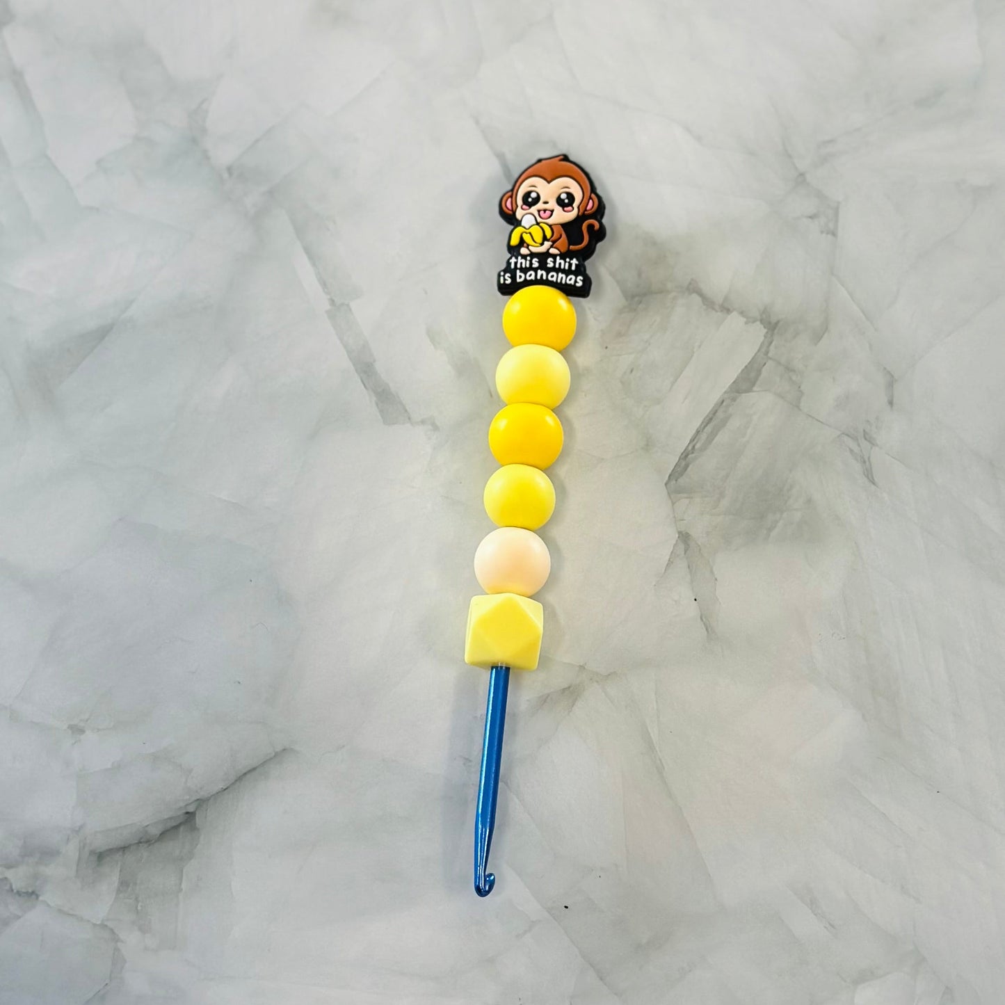 Decorative crochet hook with cartoon character and colorful beads on a marble background