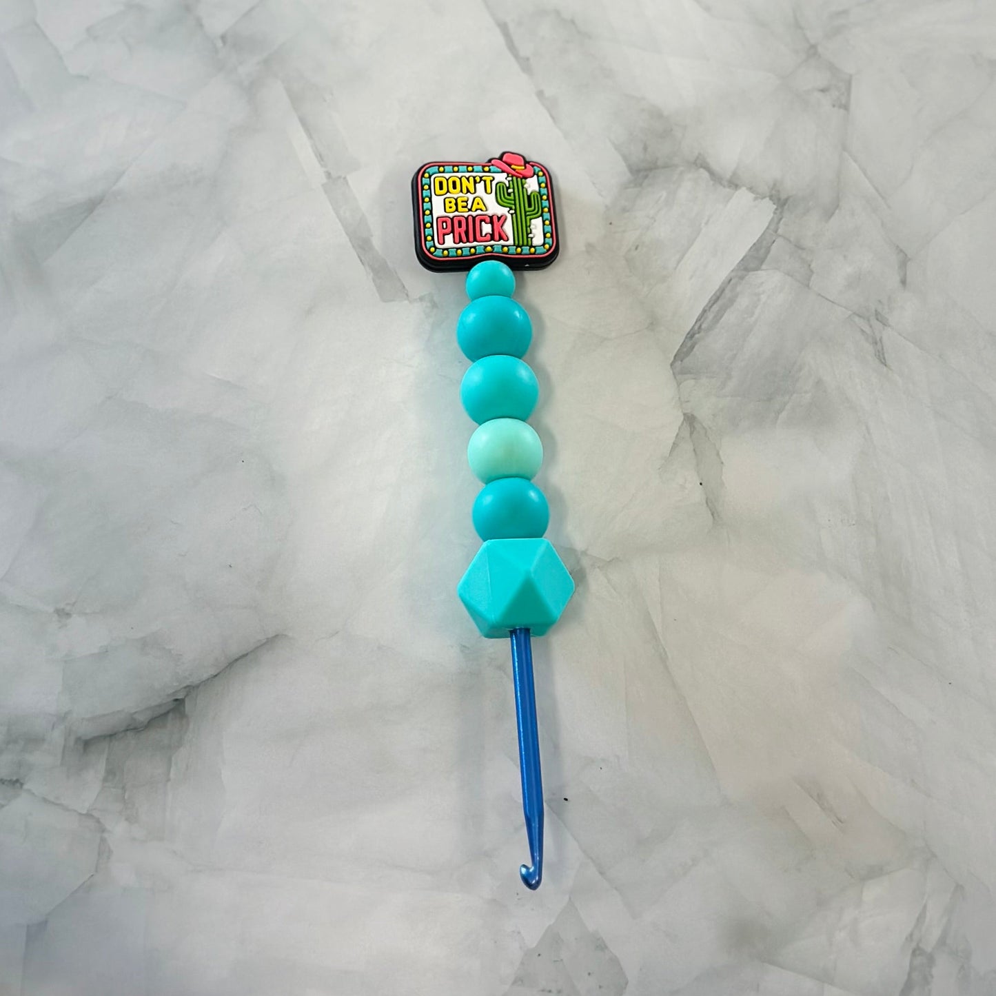 Blue crochet hook with turquoise beads on a marble surface