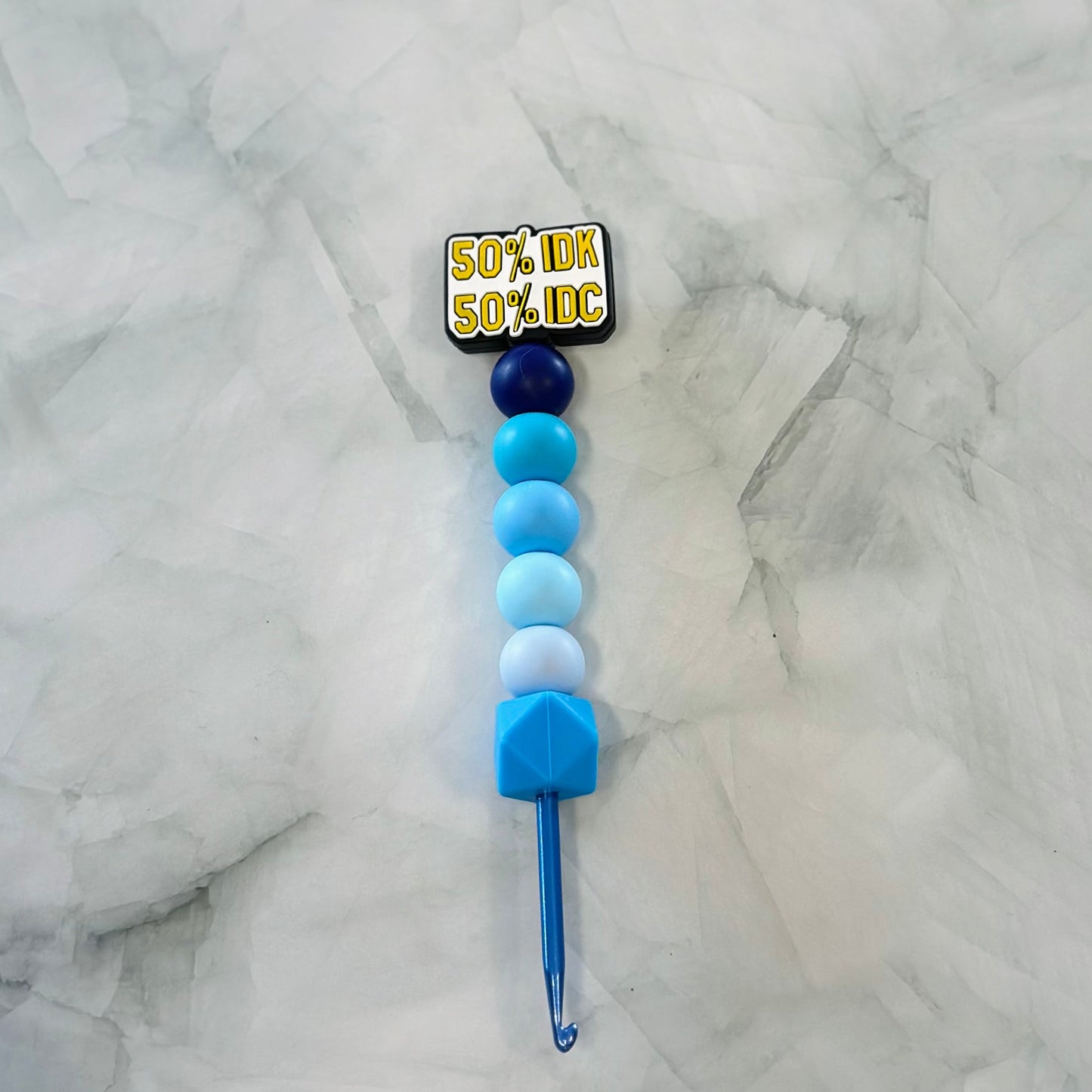 Crochet hook with colored beads on a marble surface