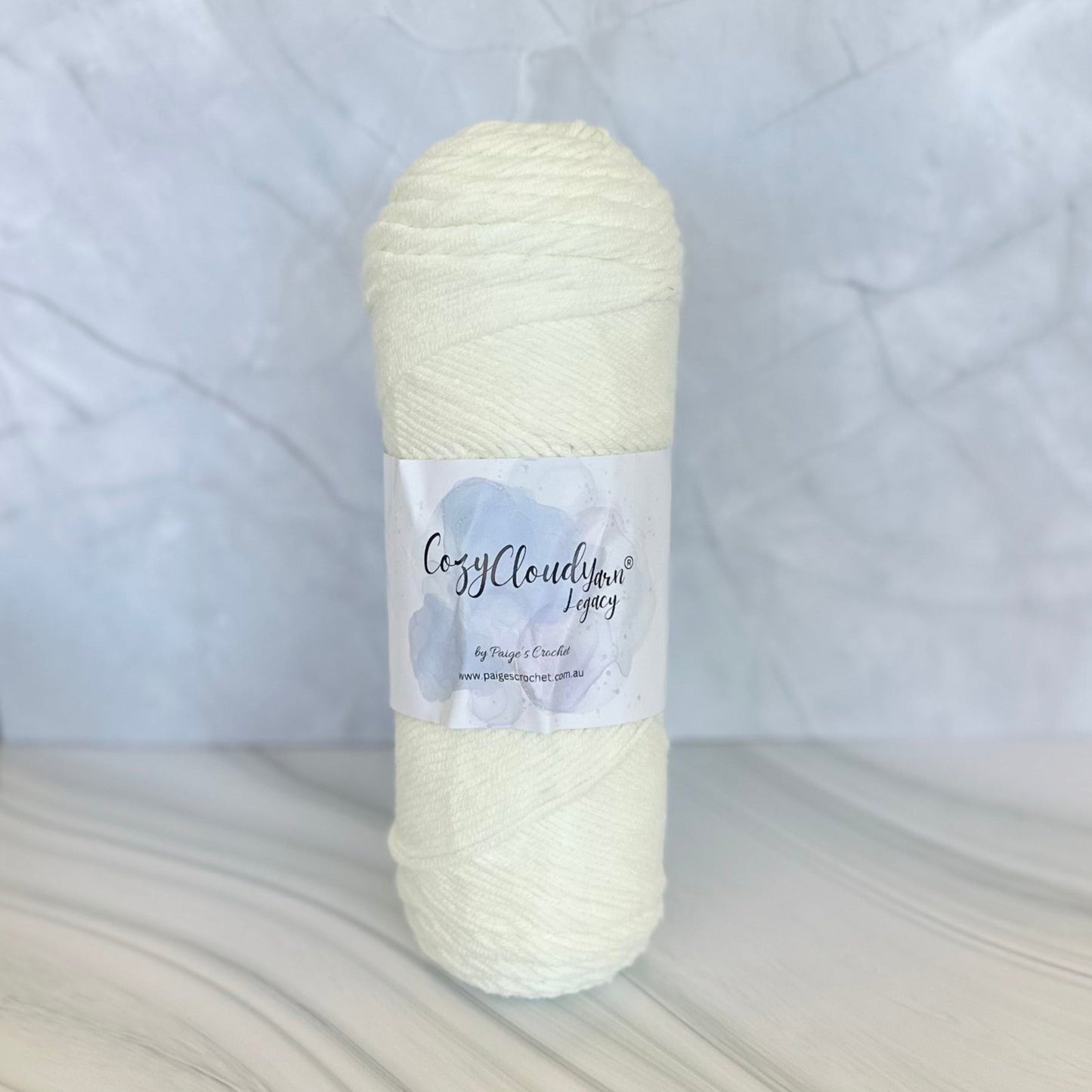 Cream-colored yarn skein with a Cozy Cloud Legacy label on a textured white background