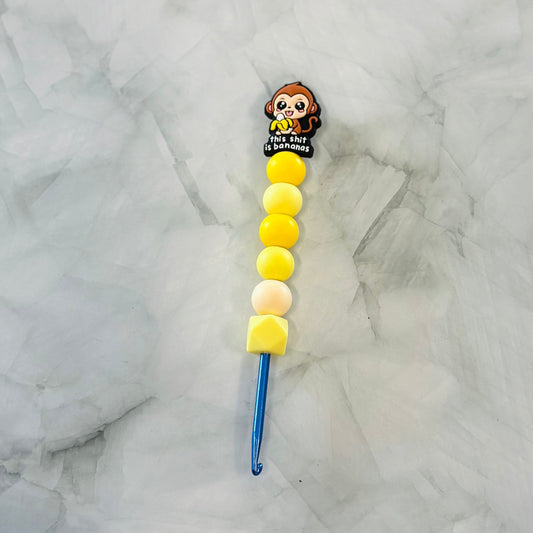 Decorative crochet hook with cartoon character and colorful beads on a marble background
