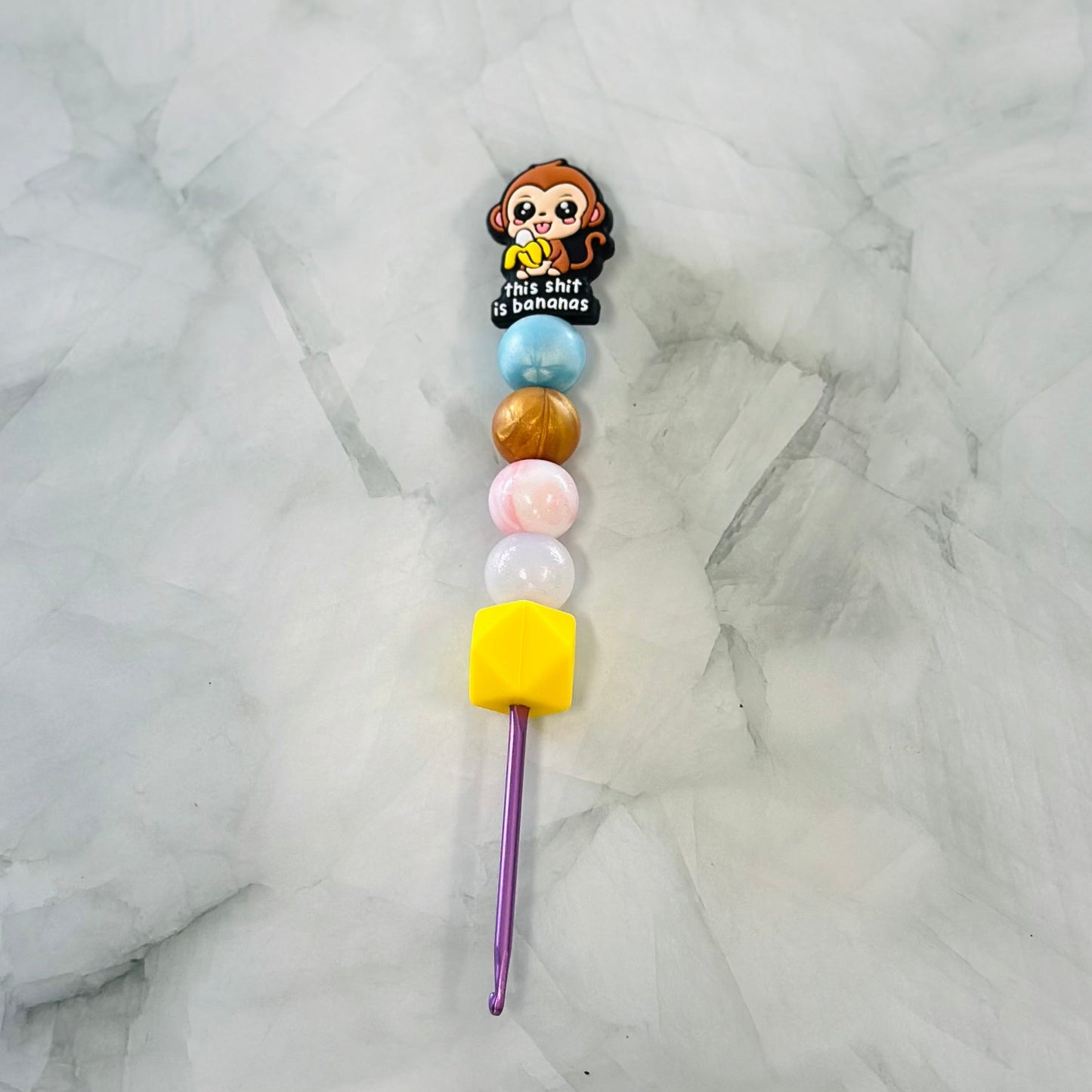 Colorful beaded crochet hook with a monkey character on a marble background for use with chenille yarn. 