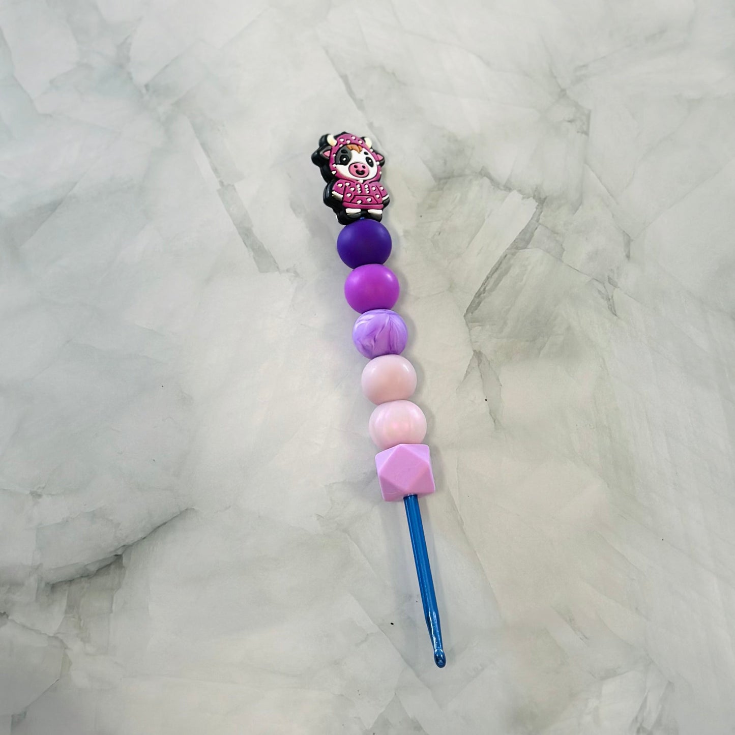 Decorative crochet hook with colorful beads on a marble surface