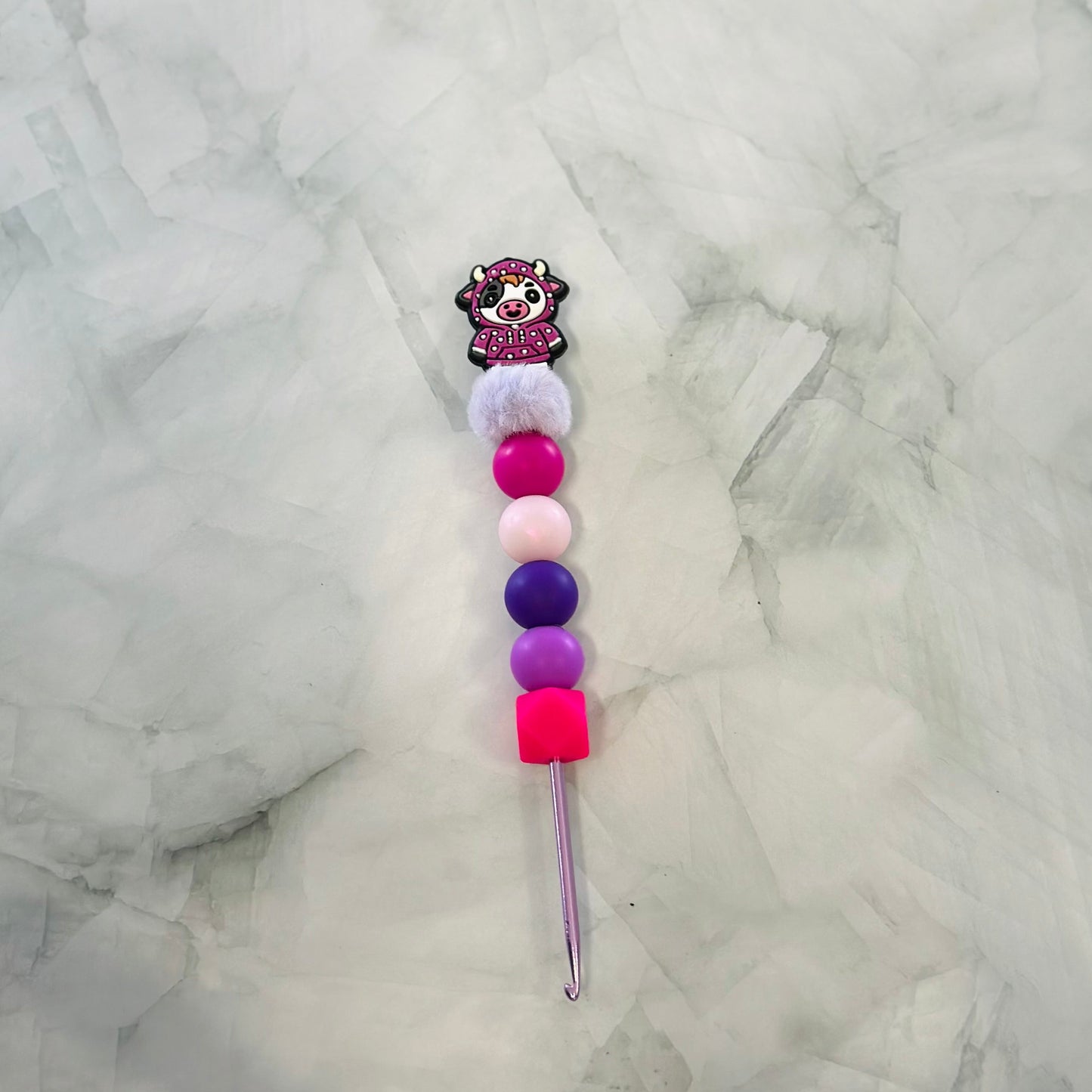 Decorative crochet hook with colorful beads and a cartoon character on a marble surface