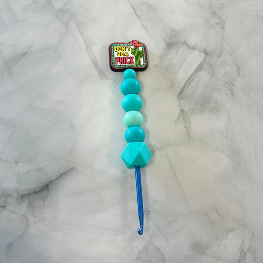 Blue crochet hook with turquoise beads on a marble surface