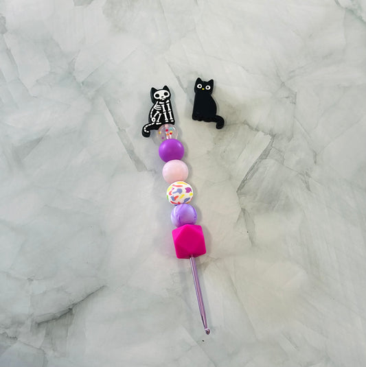 Colorful beaded tool with skeleton cat and black cat charms on a marble background