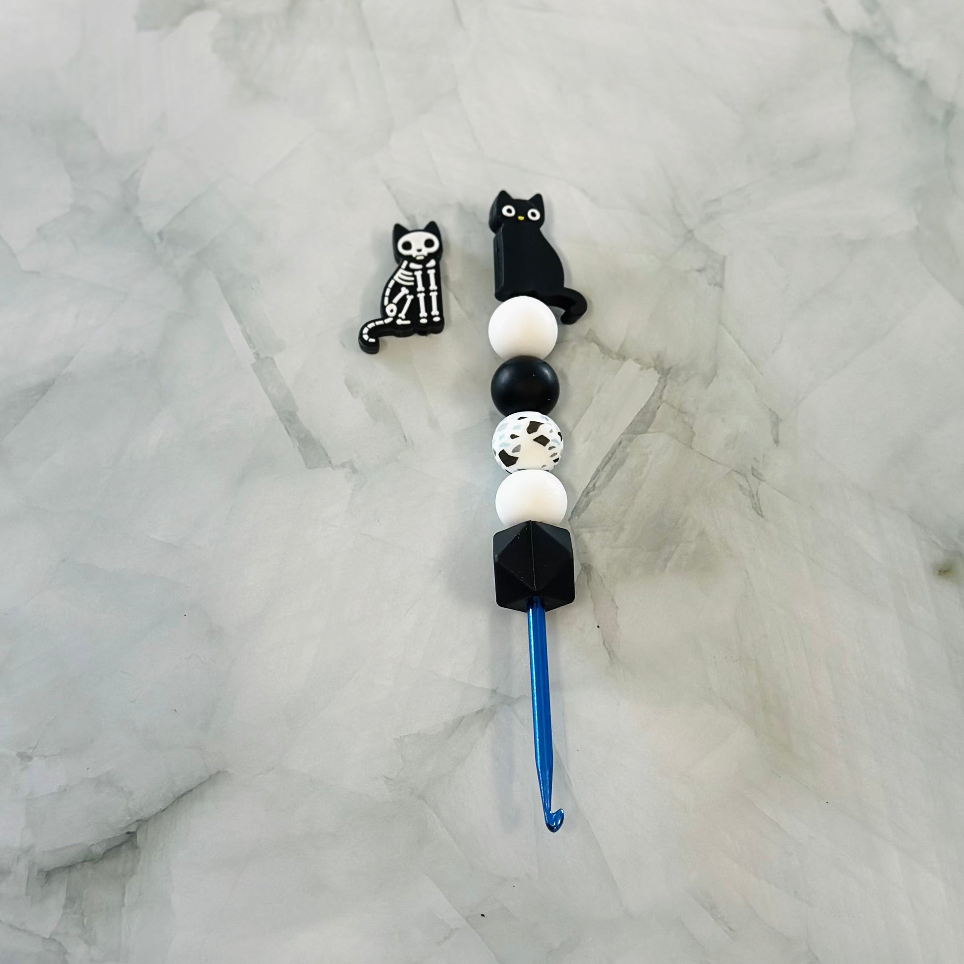 Decorative crochet hook with black cat-shaped ends on a marble surface