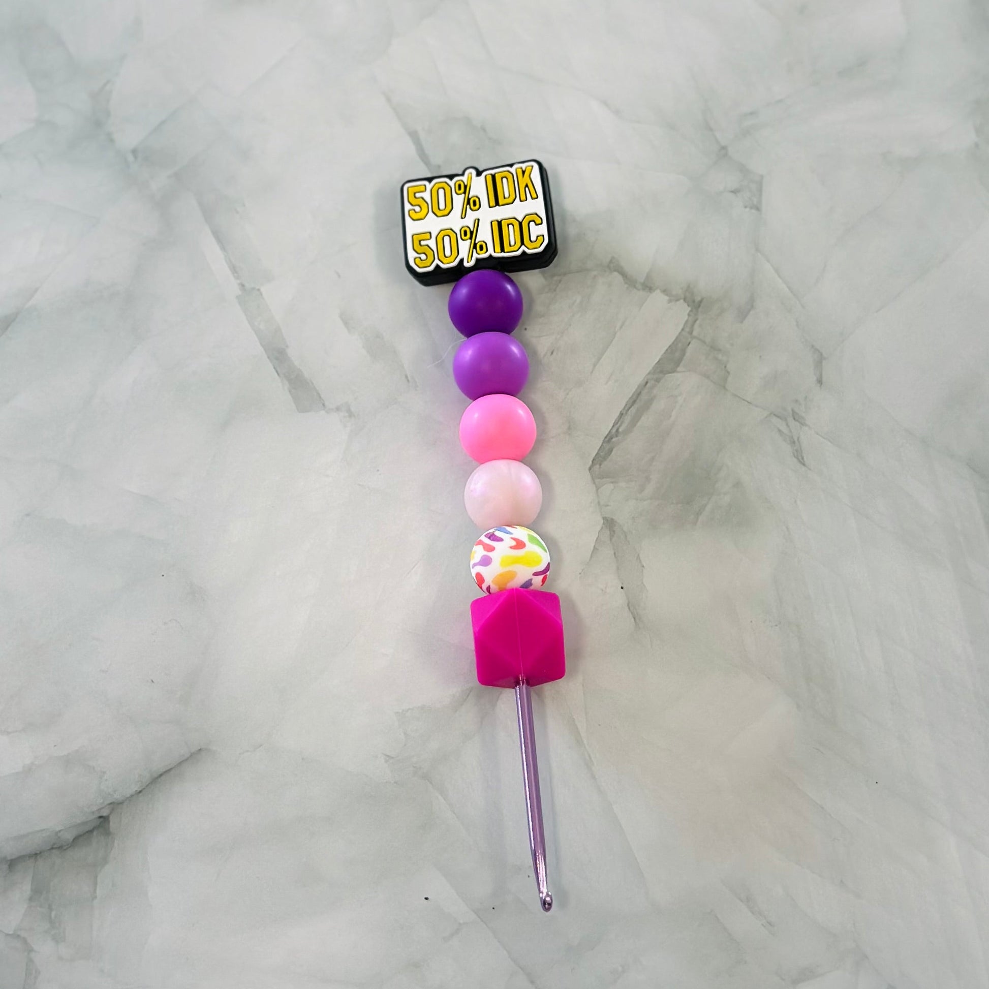 Colorful beaded crochet hook with a label on a marble surface