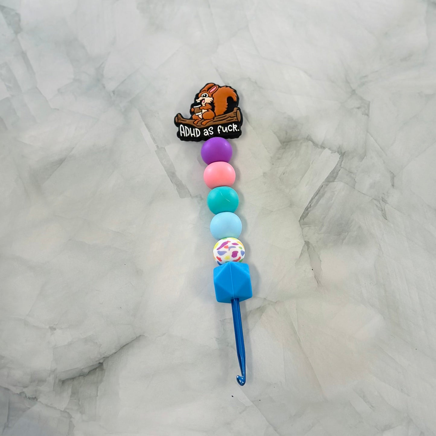 Crochet hook with colorful beads and a cartoon character on a marble background