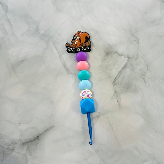 Crochet hook with colorful beads and a cartoon character on a marble background