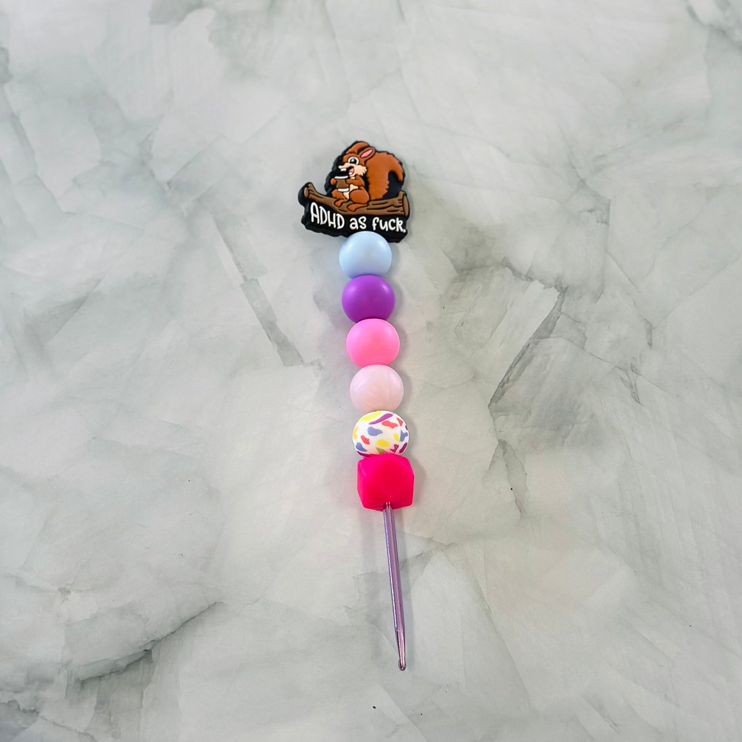 Decorative crochet hook with colorful beads and a cartoon character on a marble background