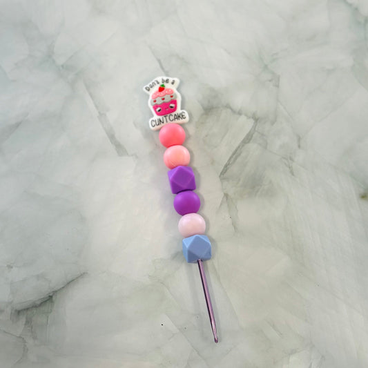 Colorful beaded crochet hook with a cartoon character label on a marble background