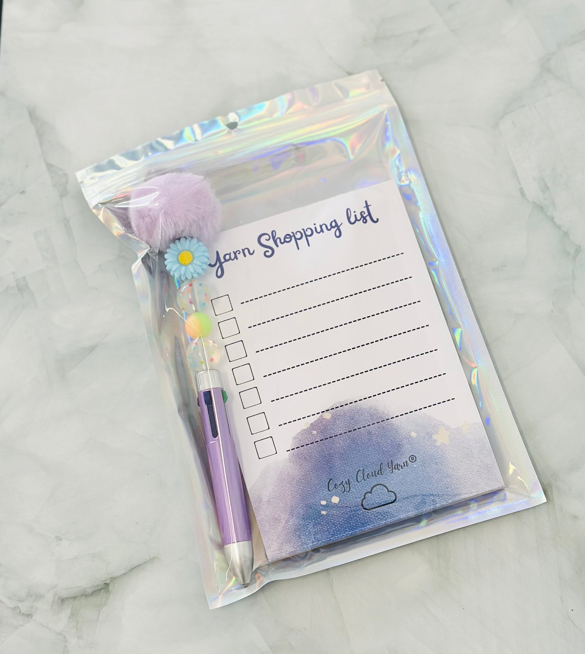 Yarn shopping list with pen and pom-pom on a marble surface