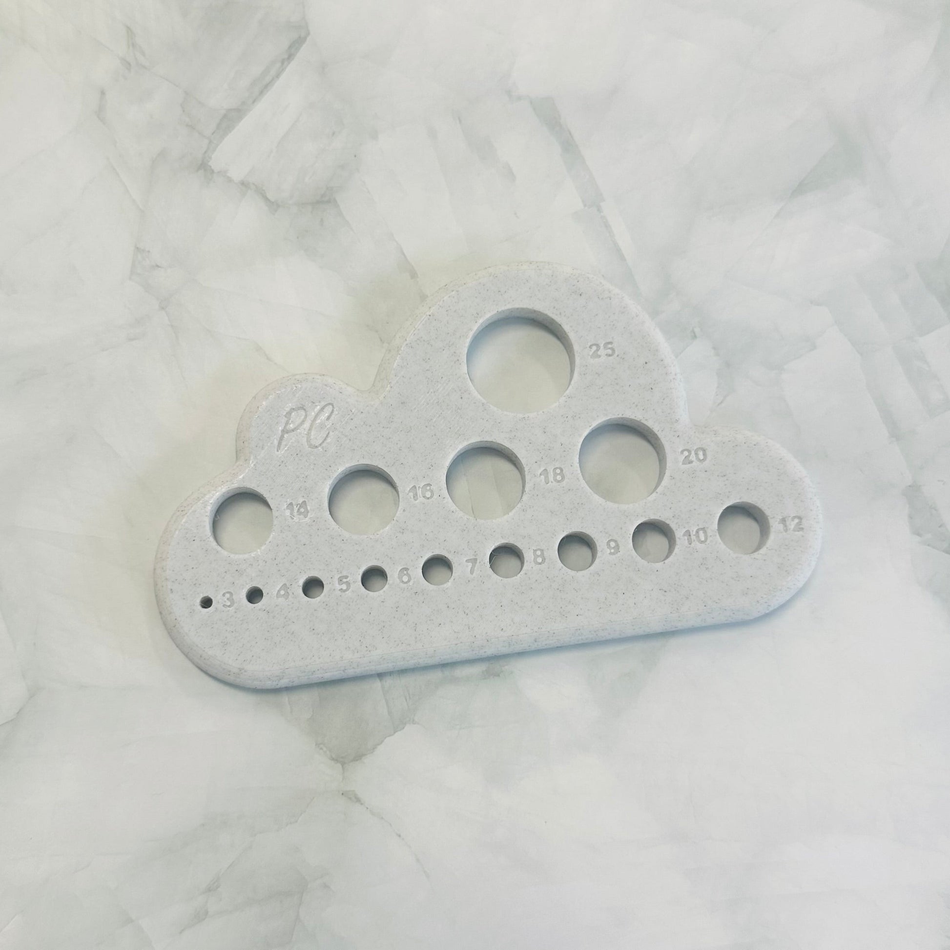 Gray plastic tool with multiple holes in it to suit plush yarn and chenille yarn. A multi tool for all crocheters 