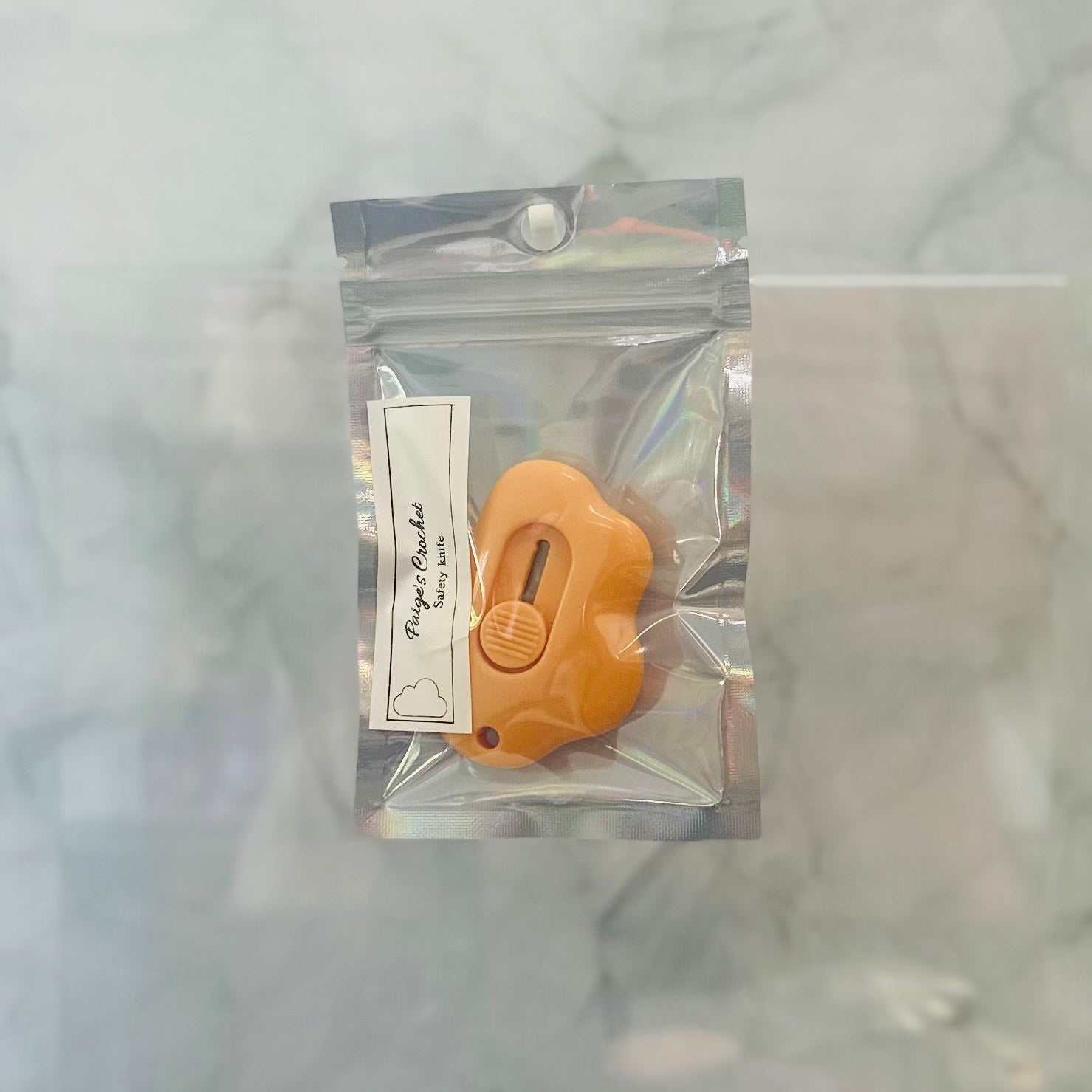 Small orange tool in a clear plastic package on a light gray background