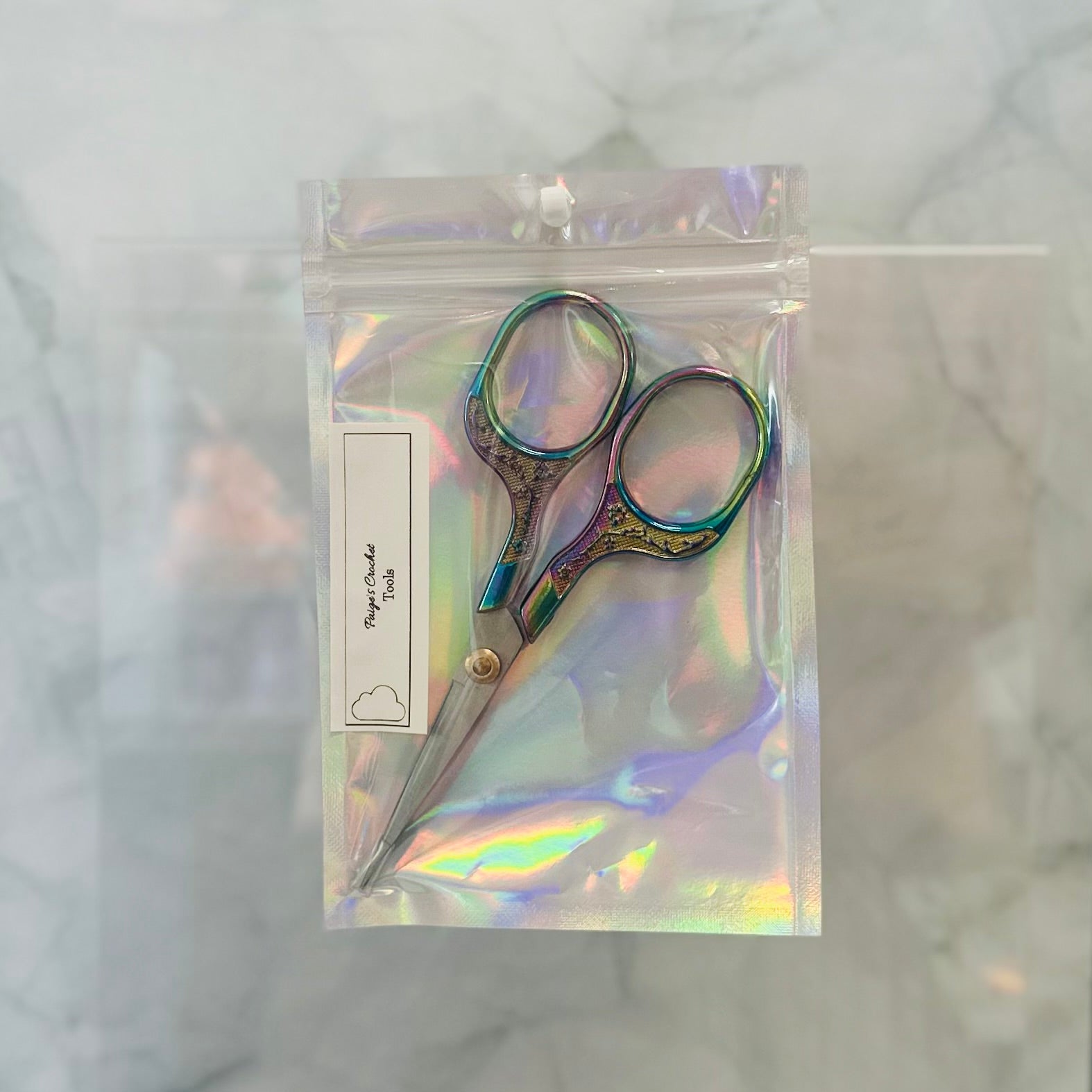 Pair of decorative scissors in a clear, iridescent packaging on a marble surface