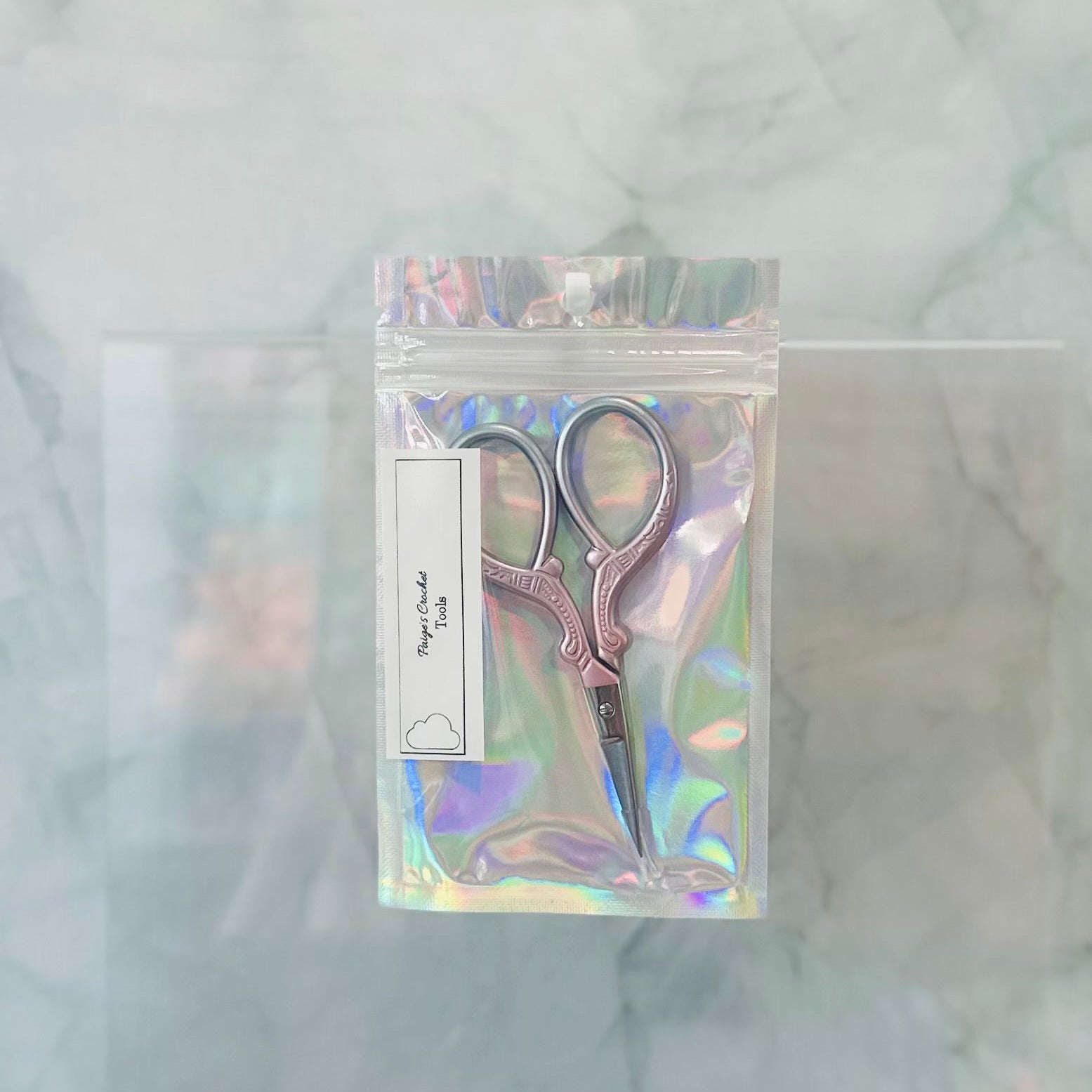 Pair of scissors in a holographic packaging on a marble surface