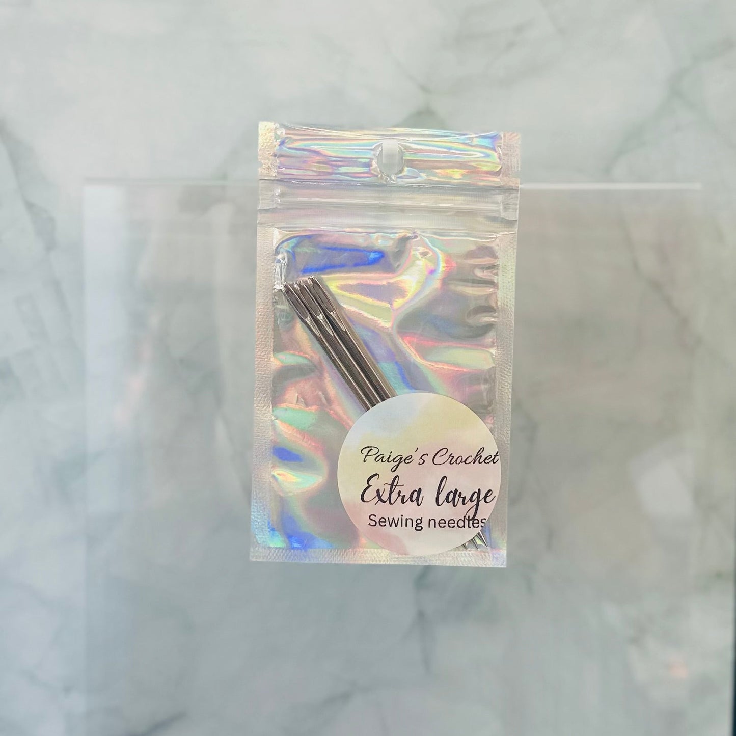 Packaged extra large sewing needles with a holographic label on a marble background
