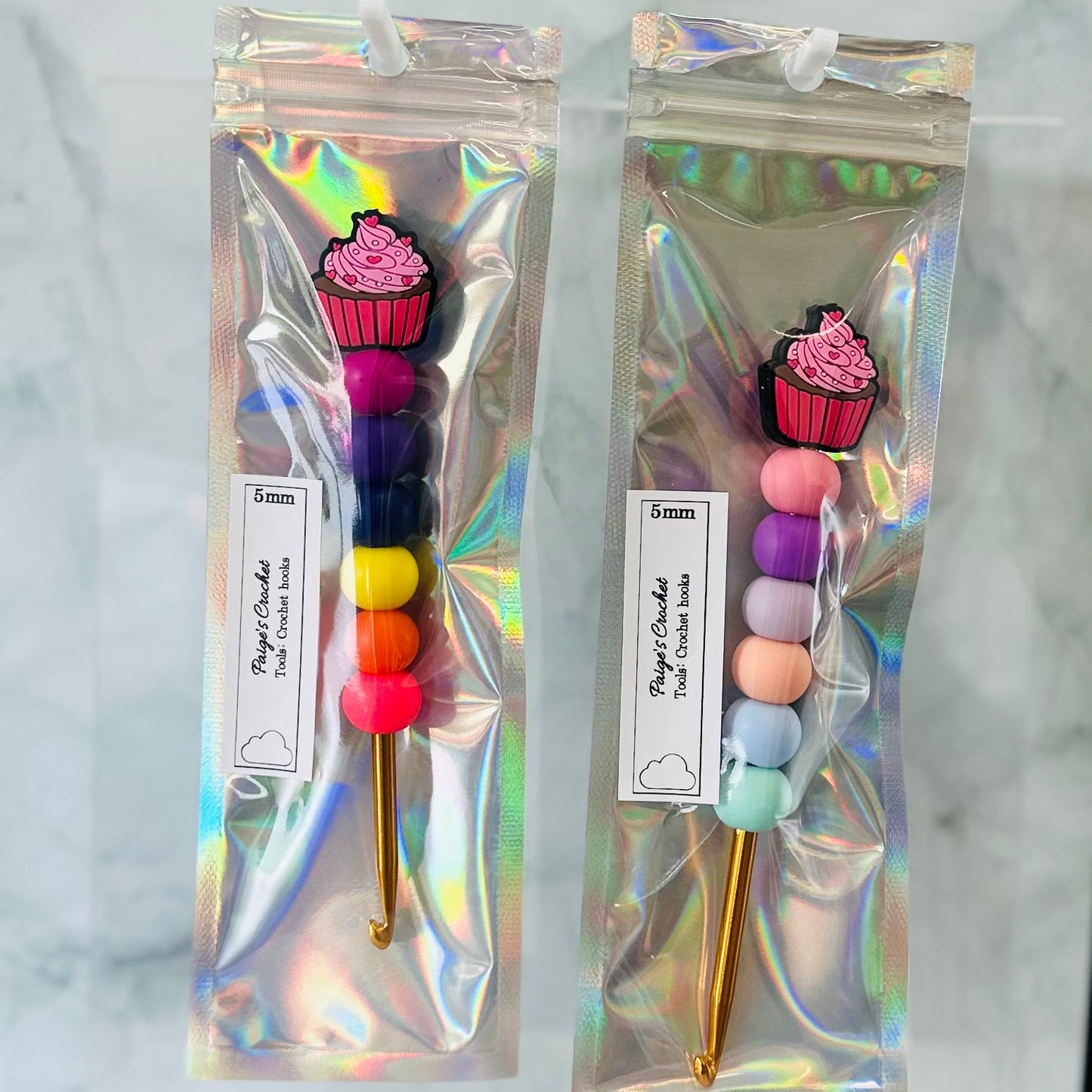 Two colorful crochet hooks with cupcake ends in clear packaging on a marble background