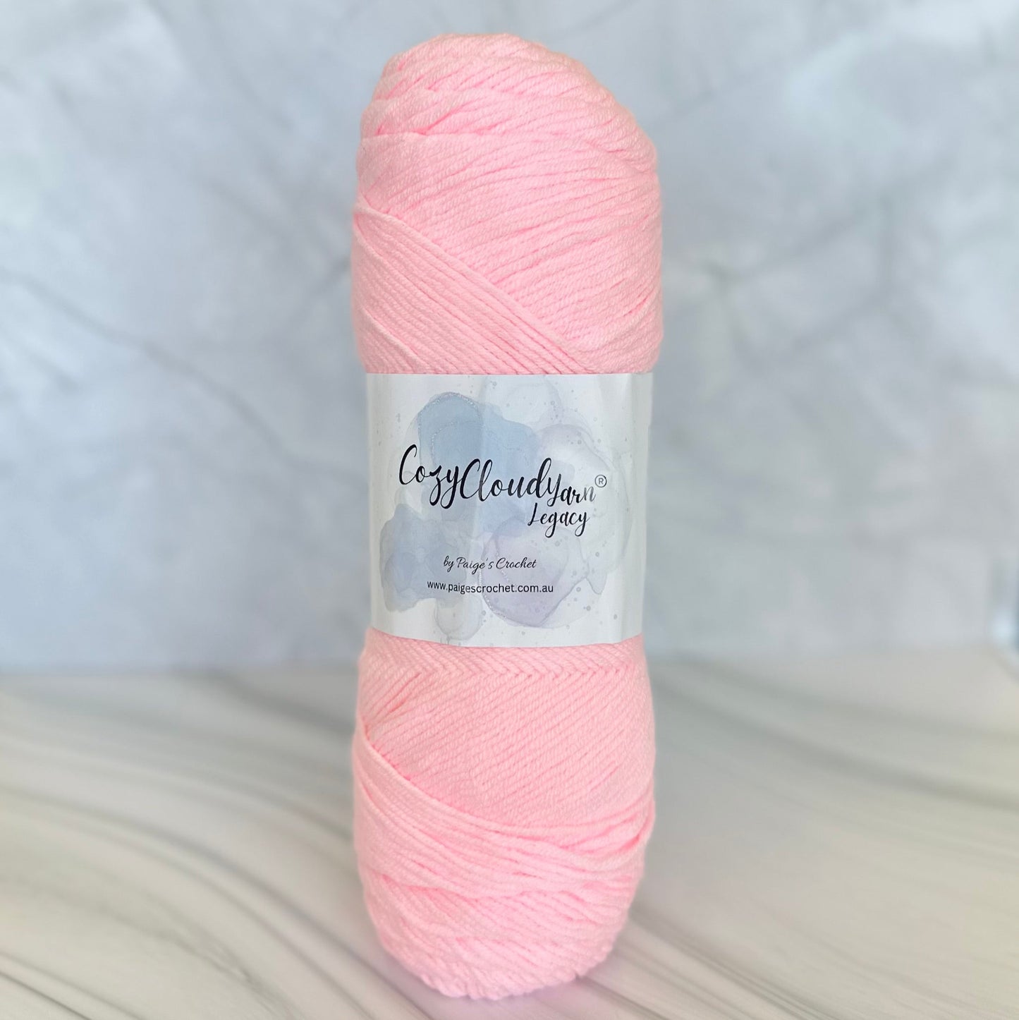 A skein of Cozy Cozy Cloud Legacy a 10 ply acrylic yarn with in a light pink colour.