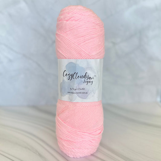 A skein of Cozy Cozy Cloud Legacy a 10 ply acrylic yarn with in a light pink colour.