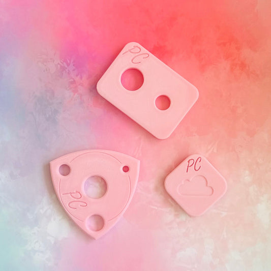 Three pink plastic pieces with cutouts on a multicolored background, This is an assistive tool to install safety eyes in hand made soft toys 