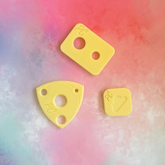 Three yellow 3d printed  plastic pieces with cutouts on a multicolored background, This is an assistive tool to install safety eyes in hand made soft toys 