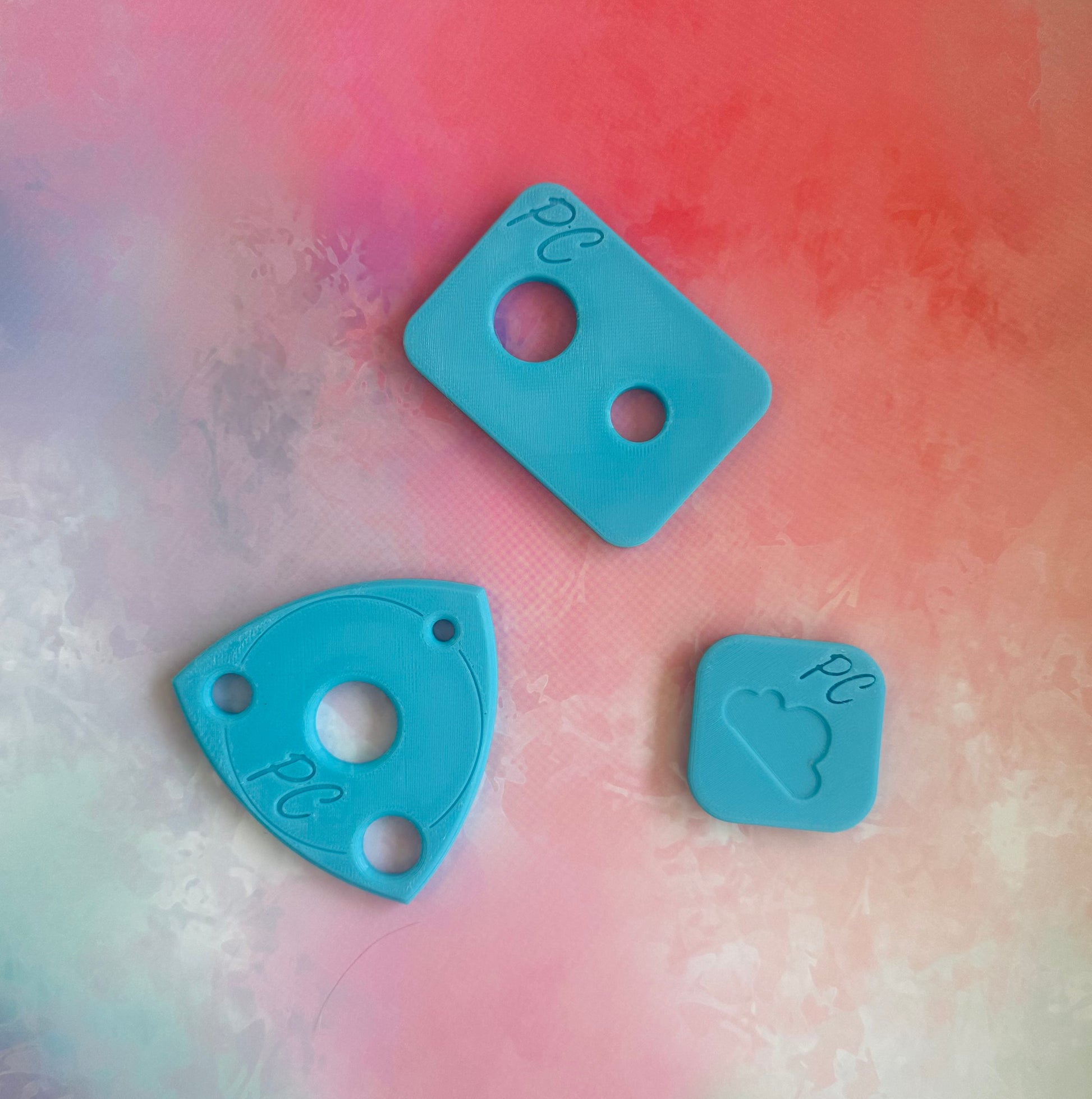 Three blue plastic pieces with cutouts on a multicolored background, This is an assistive tool to install safety eyes in hand made soft toys 